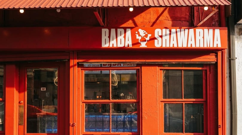 Bright red storefront of Baba Shawarma restaurant with white lettering and a cartoon logo.