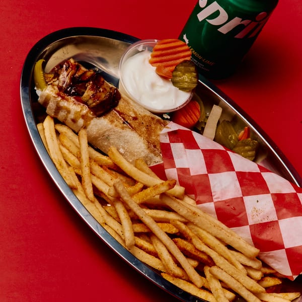 Shawarma wrap, seasoned fries, dipping sauce, and pickles on a metal tray with a Sprite can.